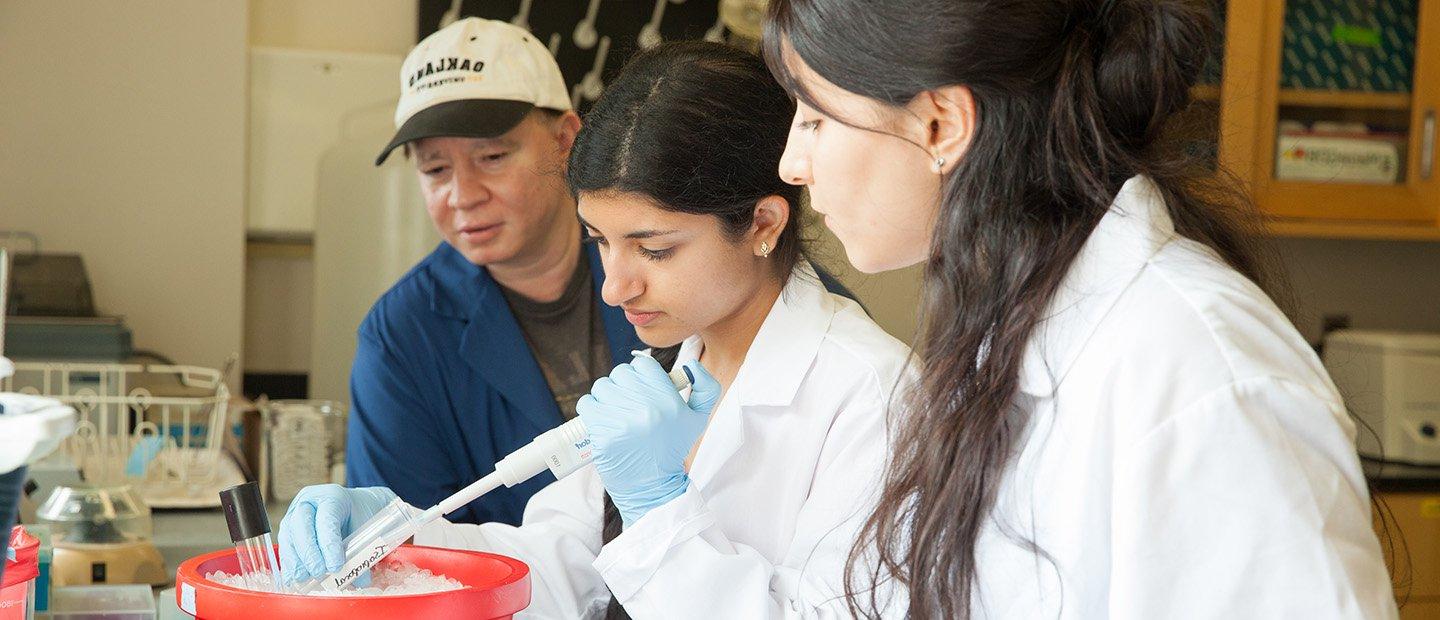 A woman holding a vial in a lab while two people observe.